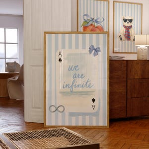 May include: Three framed art prints with a light blue and white striped background. One print features a playing card with the text "we are infinite". Another shows peaches with a blue bow, and the third shows a teddy bear wearing sunglasses and a scarf.