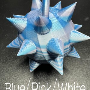 May include: A 3D printed spherical object with multiple pointed spikes, featuring a marbled colour pattern of blue, pink, and white. The surface shows visible horizontal layer lines from the printing process. Text reads Blue/Pink/White.
