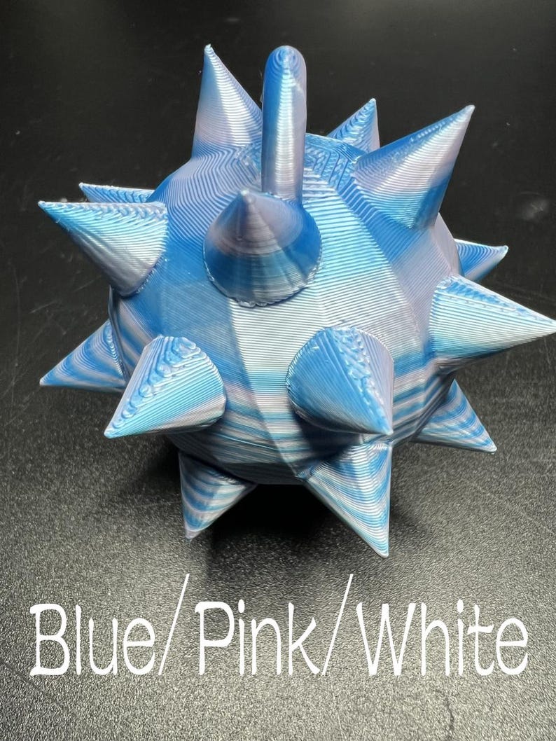 May include: A 3D printed spherical object with multiple pointed spikes, featuring a marbled colour pattern of blue, pink, and white. The surface shows visible horizontal layer lines from the printing process. Text reads Blue/Pink/White.