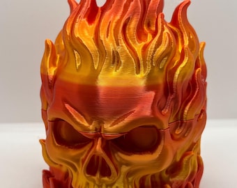 May include: A three-dimensional printed skull sculpture featuring a vibrant gradient of metallic orange, red, and yellow colors. The skull is surrounded by sculpted flames that rise from the base and extend above the top of the cranium.