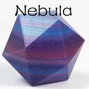 May include: A multi-faceted geometric polyhedral object with a gradient colour finish transitioning between deep purple, magenta, and blue hues. The surface features a subtle glittery texture and the word Nebula is printed above it.