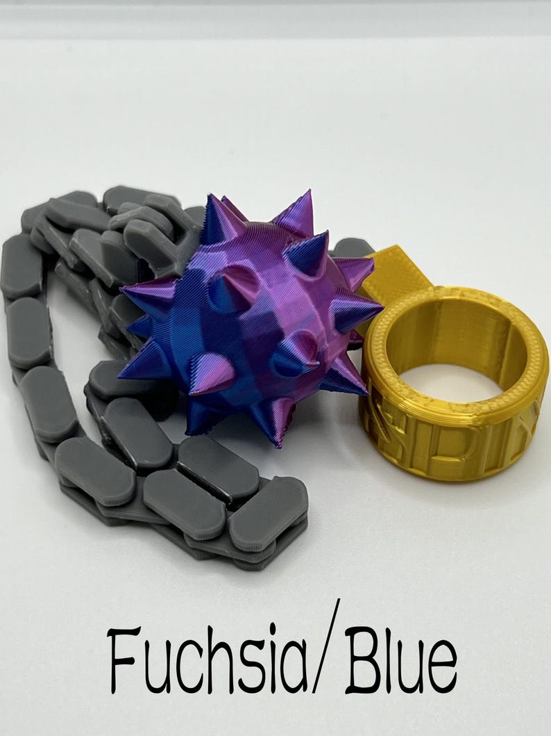 May include: A 3D-printed flail toy featuring a purple and blue spiked ball attached to a grey articulated chain and a gold ring. The text "Fuchsia/Blue" is printed at the bottom of the image. The object is composed of a spiked sphere, a flexible chain, and a circular ring component.