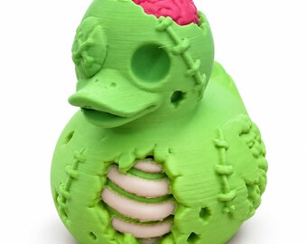 May include: A bright green rubber duck figure with a zombie-like appearance. The duck features a pink exposed brain on top of its head, one eye covered by an 'X' stitch, and a chest cavity revealing light pink ribs. Stitches are visible.