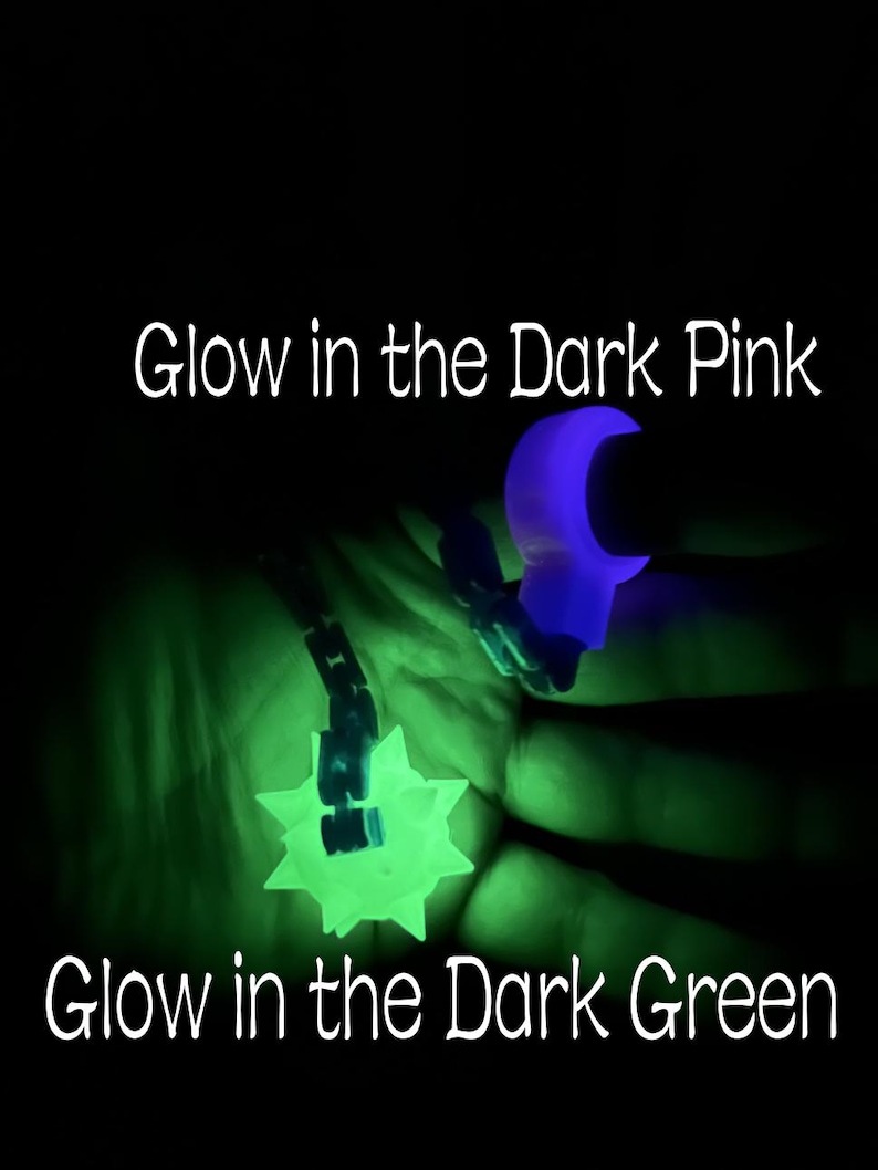 May include: A glow in the dark pink ring and a glow in the dark green spiked ball pendant on a chain. The text Glow in the Dark Pink appears at the top and Glow in the Dark Green appears at the bottom of the image against a black background.