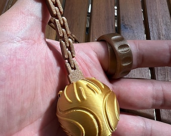 May include: A metallic gold spherical object with curved embossed lines attached to a segmented rectangular chain, accompanied by a matching gold ring featuring a series of indented oval shapes around its outer band.
