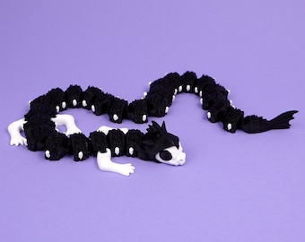 May include: An articulated dragon figurine featuring a long, segmented black body with textured scales and white accents. The creature has a white head with black eye sockets, white limbs, and a black tail fin, designed with multiple flexible joints.