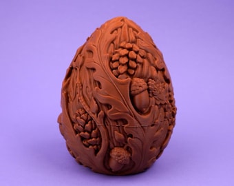 May include: A brown, egg-shaped object featuring an intricate, raised relief design of forest elements. The surface is covered in detailed carvings of oak leaves, pine cones, and acorns, creating a textured, organic appearance across the entire exterior.