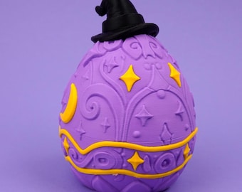 May include: A purple egg-shaped object topped with a black pointed hat. The surface features embossed swirling patterns, yellow crescent moons, and yellow four-pointed stars. A horizontal yellow band wraps around the lower section of the egg.