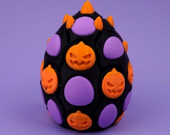 May include: An egg-shaped object with a black base featuring a repeating pattern of purple oval inserts and orange jack-o'-lantern faces. The top of the object is adorned with several small, pointed orange spikes arranged in a cluster.