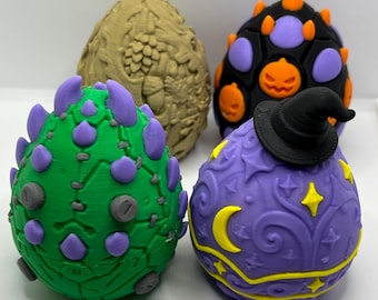 May include: Four egg-shaped objects with distinct designs. One is tan with a textured acorn pattern, one is black with purple and orange pumpkin accents, one is green with purple spikes, and one is purple with yellow stars, moons, and a black witch hat.
