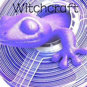 May include: A purple gecko figurine with a subtle glitter finish emerging from the centre of a coiled spool of purple and white 3D printer filament. The word Witchcraft is printed in black text above the gecko on a white background.