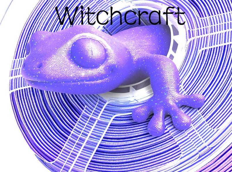 May include: A purple gecko figurine with a subtle glitter finish emerging from the centre of a coiled spool of purple and white 3D printer filament. The word Witchcraft is printed in black text above the gecko on a white background.