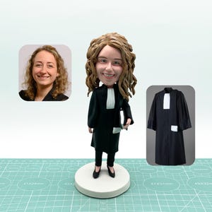Könnte beinhalten: Eine maßgefertigte Figur einer Person, die eine schwarze Anwaltsrobe mit weißem Kragen und Manschetten trägt. Die Figur hält ein Buch in der rechten Hand. Die Figur steht auf einem weißen Sockel.