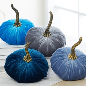 May include: Four velvet pumpkins in shades of blue and gray. The pumpkins have a ribbed texture and gold stems.