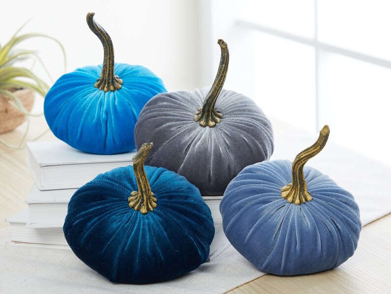 May include: Four velvet pumpkins in shades of blue and gray. The pumpkins have a ribbed texture and gold stems.
