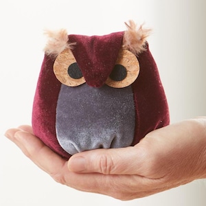 以下が含まれることがあります： ワインレッドとグレーのベルベット生地で作られた小さなぬいぐるみフクロウ。フクロウは、黒い瞳のついたコルクの目と、頭の上に羽根の房があります。