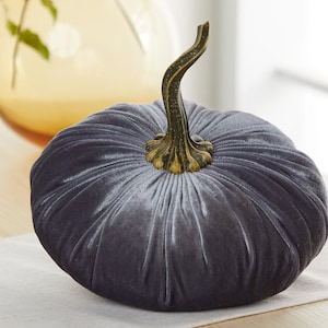 Puede incluir: Una calabaza de terciopelo gris con un tallo dorado. La calabaza es un artículo decorativo para el hogar.
