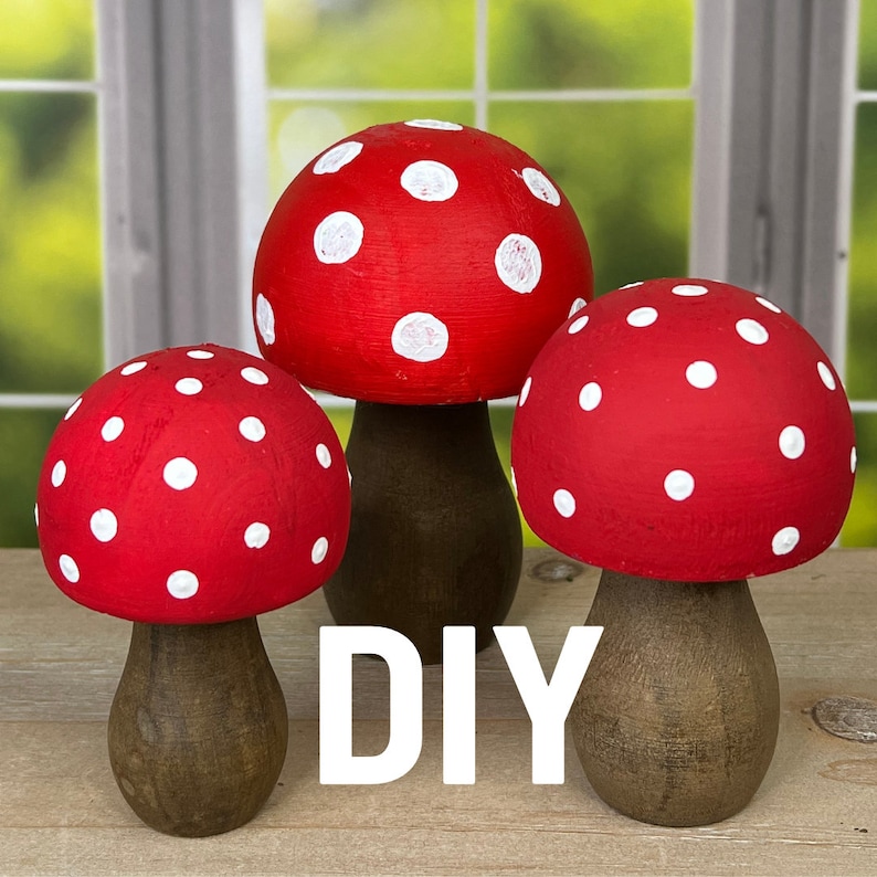 May include: Three red and white polka dot mushroom shaped ornaments with brown wooden bases. The mushrooms are arranged in a row on a wooden surface. The word "DIY" is written in white letters on the surface.