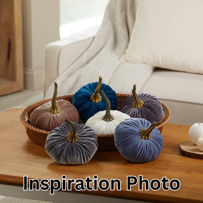 May include: Six velvet pumpkins in various colors, including blue, gray, and brown, are arranged on a woven tray. The pumpkins are decorative and have a vintage feel.