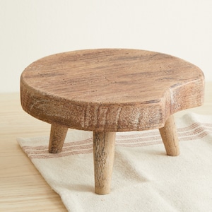 May include: A rustic wooden stool with a round top and three legs. The stool is made of natural wood and has a distressed finish.