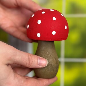 May include: A red and white mushroom shaped wooden ornament with white polka dots. The mushroom is sitting on a table.