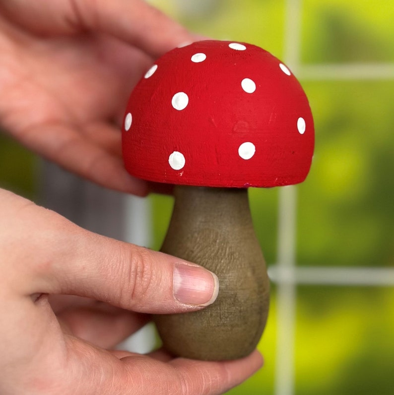 May include: A red and white mushroom shaped wooden ornament with white polka dots. The mushroom is sitting on a table.