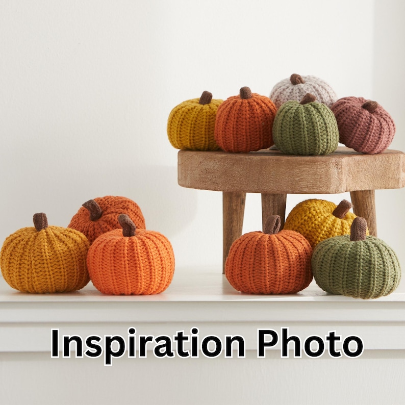 Puede incluir: Una colecci&oacute;n de calabazas de punto en varios colores, incluyendo naranja, verde, marr&oacute;n y beige. Las calabazas est&aacute;n dispuestas en un taburete de madera y una superficie blanca. El texto "Inspiration Photo" se muestra debajo de las calabazas.