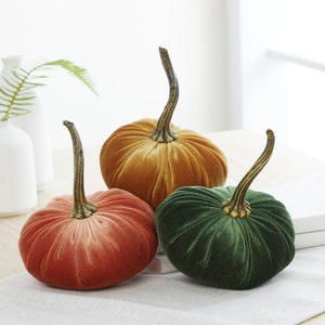 May include: Three velvet pumpkins in different colors: gold, orange, and green. The pumpkins are a decorative fall accent.