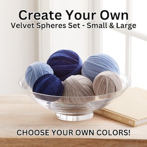 May include: A set of six velvet spheres in a glass bowl. The spheres are in various shades of blue and beige. The spheres are arranged in a decorative pattern. The bowl is sitting on a wooden table. The text "Create Your Own Velvet Spheres Set - Small & Large" is at the top of the image. The text "CHOOSE YOUR OWN COLORS!" is at the bottom of the image.