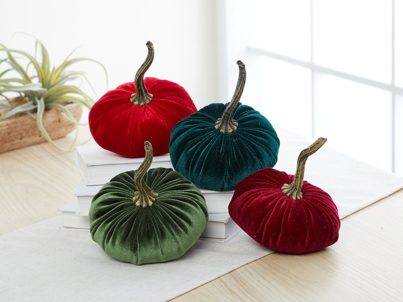 Op de afbeelding: Vier fluwelen pompoenen in rood en groen. De pompoenen zijn decoratief en hebben een steel.