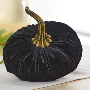 May include: A black velvet pumpkin with a gold stem. The pumpkin is sitting on a white surface.