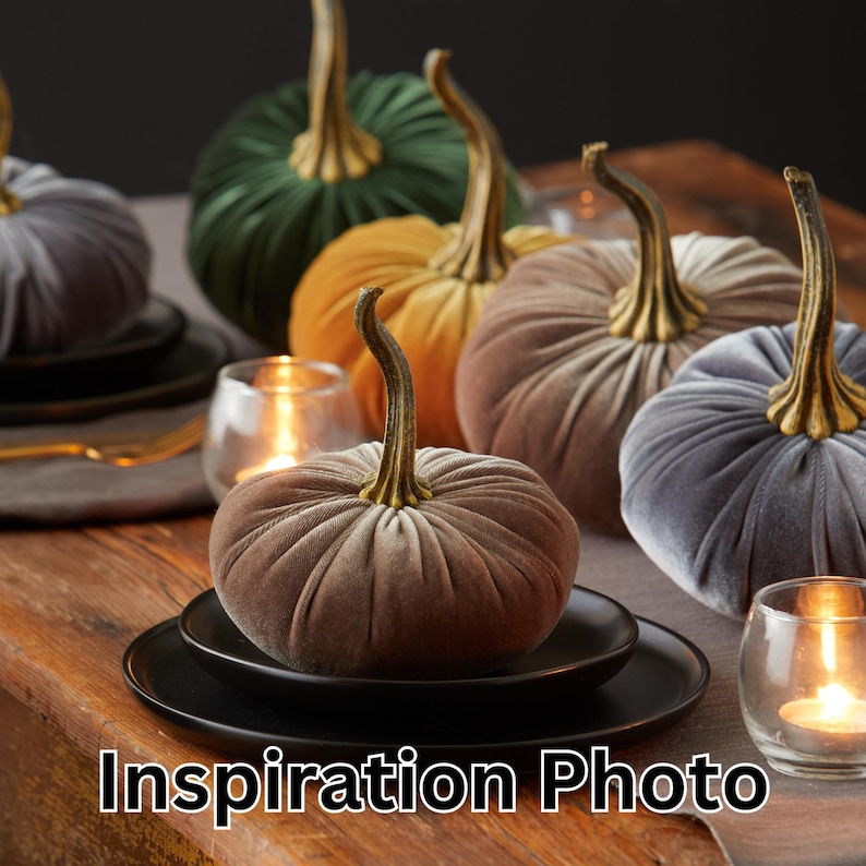 May include: Velvet pumpkins in shades of green, gold, grey, and brown, each with a gold stem, are displayed on a wooden table. Black plates and lit candles add to the autumnal theme. The image includes the text "Inspiration Photo" at the bottom.