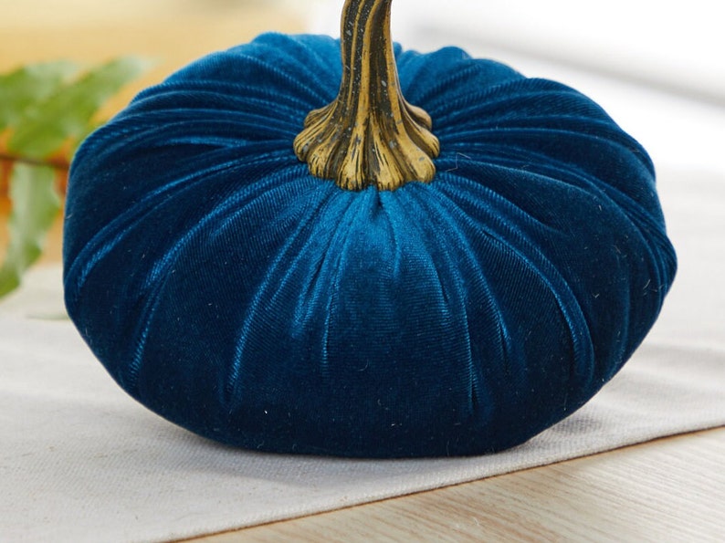 May include: A teal blue velvet pumpkin with a gold stem. The pumpkin is a decorative item for fall and autumn.