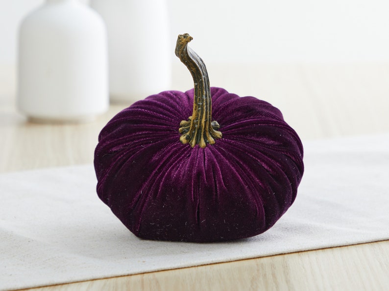 K&ouml;nnte beinhalten: Ein tiefschwarzer Samt-K&uuml;rbis mit goldenem Stiel. Der K&uuml;rbis ist ein Dekorationsartikel f&uuml;r Herbst und Halloween.