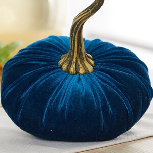 May include: A teal blue velvet pumpkin with a gold-colored stem. The pumpkin is a decorative item for fall and autumn.