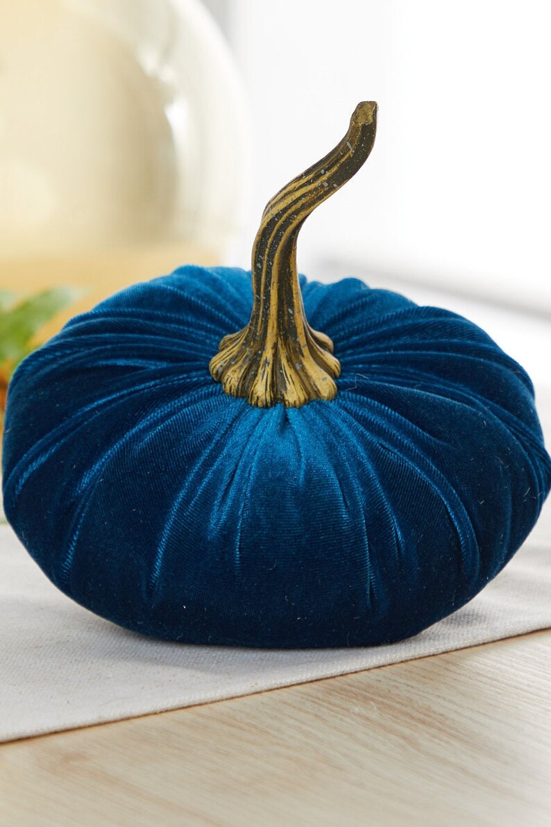 May include: A teal blue velvet pumpkin with a gold-colored stem. The pumpkin is a decorative item for fall and autumn.