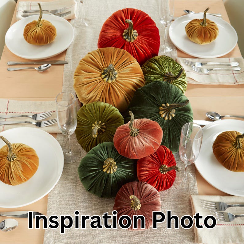May include: A table setting featuring a centrepiece of velvet pumpkins in a variety of colours, including red, green, orange, and pink. The pumpkins are arranged in a cascading pattern, with the largest pumpkin at the top and the smallest pumpkins at the bottom. The table is set with white plates, cutlery, and glasses.
