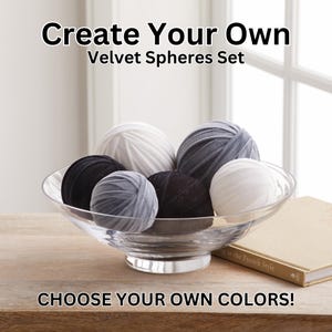 May include: A set of six velvet spheres in a clear glass bowl. The spheres are in various colors, including white, gray, and black. The text "Create Your Own Velvet Spheres Set" and "CHOOSE YOUR OWN COLORS!" is visible in the image.