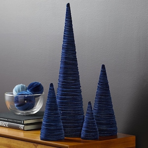 May include: Four blue velvet cone-shaped Christmas trees of varying sizes on a wooden surface.