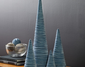 May include: Four blue velvet cone-shaped Christmas trees of varying sizes. The trees are arranged on a wooden surface.