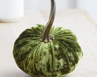 May include: A green velvet pumpkin with a brown stem. The pumpkin is a decorative item for fall and autumn.