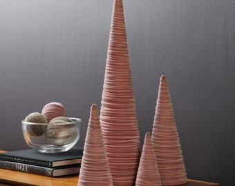 May include: Set of three pink velvet cone-shaped Christmas trees of varying sizes. The trees are arranged on a wooden surface.