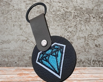 This is a blue diamond embroidered patch on a black leather keychain.