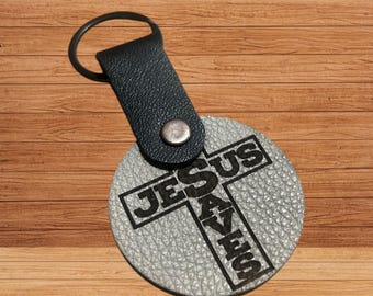 This is a black and silver leather keychain featuring a laser-engraved cross with the text "Jesus Saves"