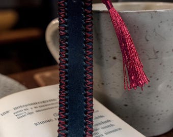 This is a handcrafted black leather bookmark featuring red stitching and a red tassel.