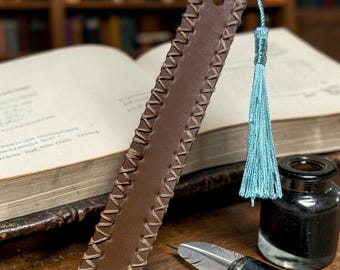 This is a brown leather bookmark featuring a whip-stitched edge and a light blue tassel.