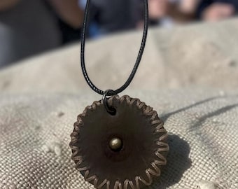 This is a handmade circular pendant necklace featuring a black gunmetal-toned saw blade design with a central stud on a thin dark cord.