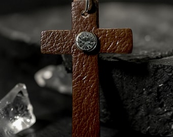 This is a Western-style leather cross pendant featuring a textured brown finish and a central rhinestone concho embellishment.