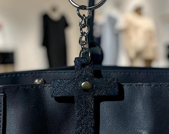 This is a black textured leather cross bag charm with a gold-tone rivet and silver key ring.