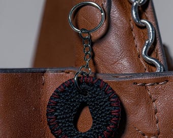 This item is a handmade black and red keychain featuring a textured, circular pendant with a central tear-drop shape